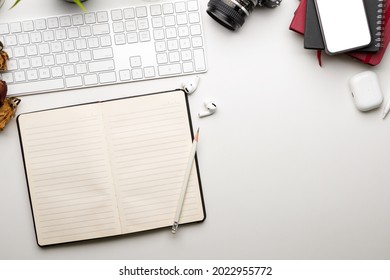 Flat lay, Minimal workspace with opened blank notebook, copy space on white table, keyboard, camera, blank screen phone mockup on books