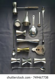 Flat Lay Of Mixologist Tools Made Of Shiny Metal, Resting On A Dark Grey Cloth