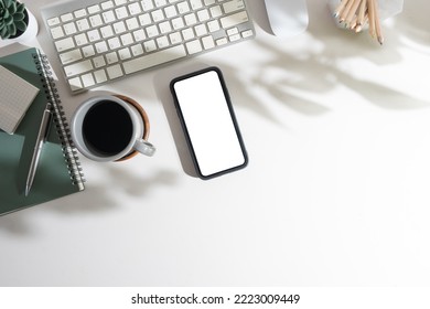 Flat lay mobile phone with empty screen, coffee cup, notepad and keyboard on white table. Top view with copy space. - Powered by Shutterstock