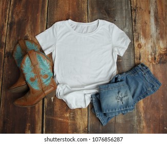 Flat Lay Mockup Of White T Shirt On Rustic Wood Background With Cowboy Boots And Ripped Jeans