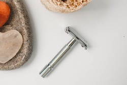 Flat Lay Of Modern Sustainable Beauty Products Highlighting A Silver Safety Razor, And Part Of Heart Shaped Himalayan Salt Massage Stones And A Natural Plant-based Loofah Exfoliating Sponge. 