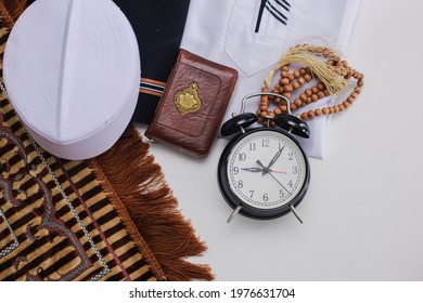 Flat lay of muslim dressed and accessories for salat, Holy Quran and prayer beads with alarm clock showing Duha time pray. There is Arabic word which means Holy Book - Shutterstock ID 1976631704