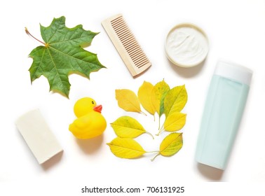 Flat Lay Natural Bath Products. Autumn Hair And Body Care. Baby Soap, Shampoo Bottle, Wooden Comb, Body Cream, Yellow And Green Leaves And Rubber Duck On A White Background. Flat Lay Photography