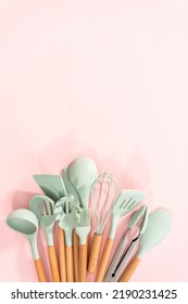 Flat lay. New blue silicone kitchen utensils with wooden handles on a pink background.