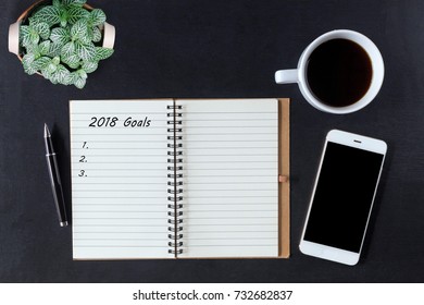 Flat lay of notebook with action 2018 goals and smartphone, on black office desk. Office desk on top view.