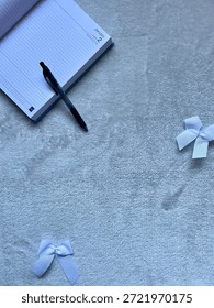 Flat Lay On A Fluffy Background With A Diary In The Corner With A Pen Laid On Top With Bow Accessories Dotted Around. 