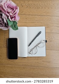 Flat Lay Open Notebook With Pen And Glasses Resting On Wooden Surface With Mug And Pink Rose