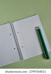 Flat Lay Of Open Spiral  Notebook With Green Coloured Pencils On Mint Background With Copy Space.
