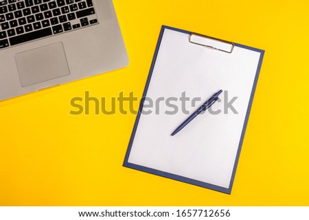 Flat lay out. Computer on yellow background with paper folio and pen. Business concept idea. Copy space.