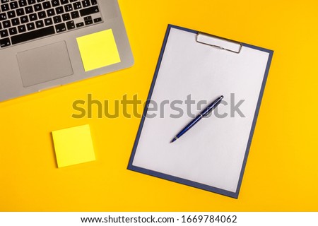 Flat lay out. Computer on yellow background with paper folio, pen and sticky notes. Business concept idea. Copy space.