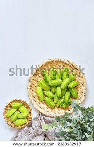 flat lay overhead top view green bilimbi kamias fruit in bamboo plate on white wood table background. green bilimbi kamias on white background. green bilimbi kamias on white food table light mood  