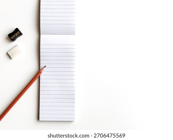 Flat Lay Overhead View Of Lined Notepad With Pencil And Basic Stationery On White Background
