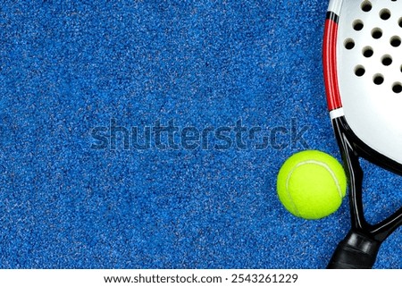 Flat lay of a padel ball and racket on the blue court background with copy space.