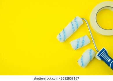Flat lay of a paint roller with multiple replacement heads and masking tape arranged on a bright yellow background, top view, with space on the left side for text