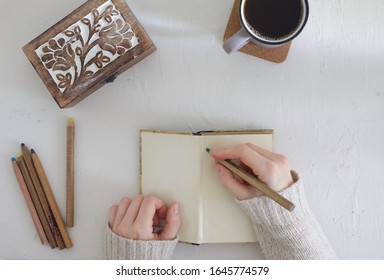 Flat Lay Pale Higgle Concept Image Of Girl Blogger In Knitted Pull Over, Drawing, Journaling Or Writing Memoir With Black Coffee And Different Colour Pens.