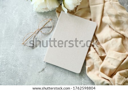 Flat lay paper notebook, eyeglasses, peony flowers and beige cloth on stone background. Top view girl home office desk with elegant accessories. Modern feminine workspace concept