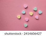 flat lay of pastel colorful candy hearts against a pink background with copy text and copy space 