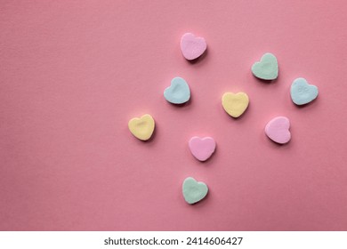 flat lay of pastel colorful candy hearts against a pink background with copy text and copy space 