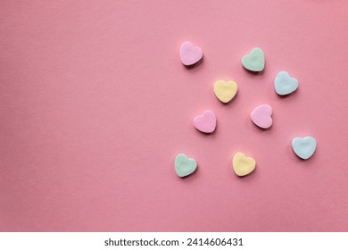 flat lay of pastel colorful candy hearts against a pink background with copy text and copy space