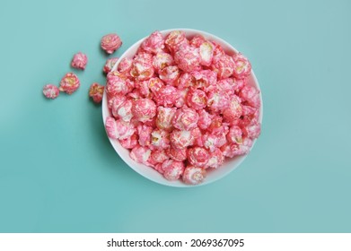 Flat lay photo of sweet pink candy (cherry, strawberry, bubble-gum flavor) popcorn in a bowl at blue background.