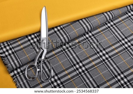 Flat lay photography of plaid  pattern fabric for suits with yellow accent line. On top of it is a solid color yellow suit fabric and sewing scissors.