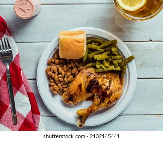 Flat Lay Of Picnic Barbecue  With Chicken, Baked Beans, Green Beans, Roll And Sweet Tea.