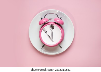 Flat lay of pink alarm clock on white plate with spoon and fork as clock hand on pink background. Ketogenic dieting, weight loss, meal plan, Intermittent fasting, and healthy food concept - Shutterstock ID 2213311661