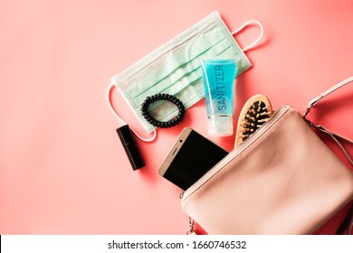 Flat Lay Of Pink Leather Woman Bag Open Out With Face Mask ,sanitizer Hand Gel To Protect From Coronavirus Or COVID-19, Lipstick, Accessories And Smartphone On Pink Background With Copy Space