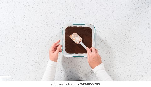 Flat lay. Pouring fudge mixture into the baking pan lined with parchment paper to prepare chocolate peanut butter fudge. - Powered by Shutterstock