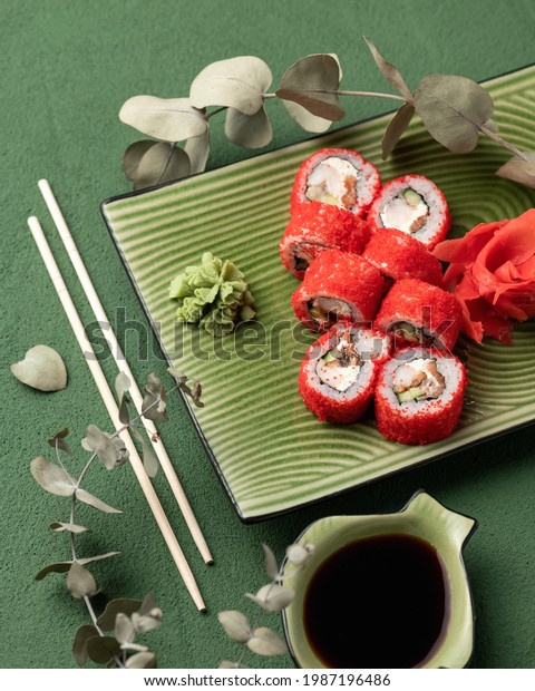 Flat lay. Red Sushi roll in masago or tobiko\
caviar. Inside-out Sushi Set on green background. Bright colors.\
Classic Japanese food. Healthy Oriental meall. Top view. Soft\
focus. Vertical format.
