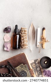 Flat lay of ritual tools including crystals, tarot cards, a candle, sage, feather, dropper bottle, and leather journal on a stone surface. Ideal for spiritual or metaphysical themes.