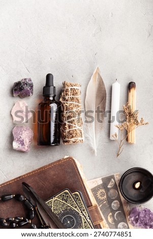 Flat lay of ritual tools including crystals, tarot cards, a candle, sage, feather, dropper bottle, and leather journal on a stone surface. Ideal for spiritual or metaphysical themes.
