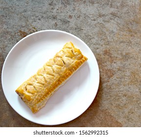 Flat Lay Of Sausage Roll On A White Plate On A Plain Brown Background With White Space