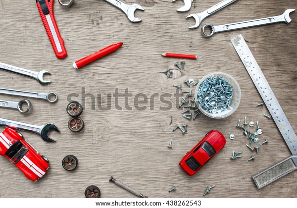 Flat lay of set of tools\
for car repairing on wooden background with contrast red toy cars.\
Top view.