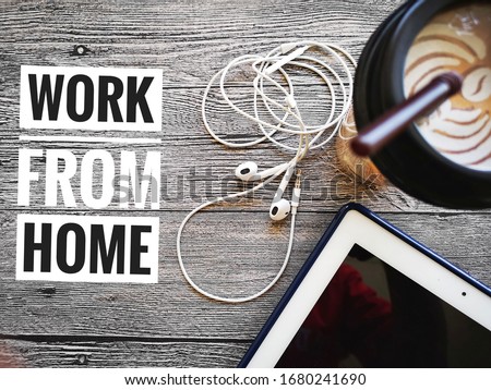 flat lay shot concept a word - WORK FROM HOME and earphone/drink cup/phone over wooden background with selective focus. 