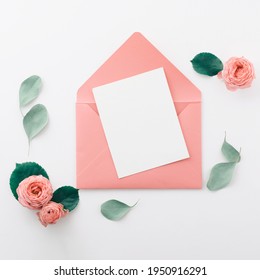 Flat lay shot of letter and envelope on white background. Wedding invitation cards or love letter with pink roses. Valentine's day or mother day holiday concept, top view, flat lay, overhead view
