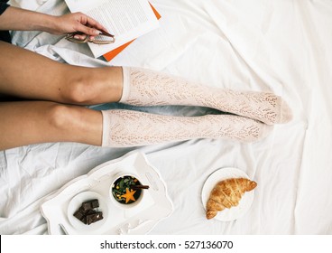 Flat Lay Shot Of Soft Photo Of Woman On The Bed With Cup Of Herbal Tea Reading Book, Top View Point