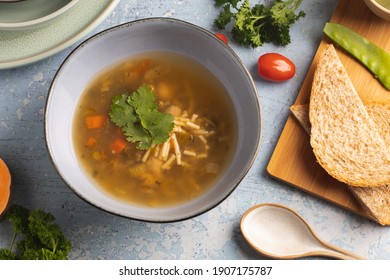 Flat Lay Shot Of Vegetable Soup, With Corriander, Tomato, Bread And Ceramic Spoon On Blue Rustic Background 