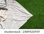 Flat lay shot of white blanket lies on green grass, creating a simple and elegant scene. Garden with plaid and decorative cushion on lawn. Recreation area on backyard. Summer vacation concepts