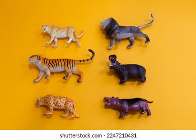 Flat lay side view of small toys in the shape of African animals set on plain orange background