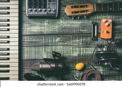 Flat lay singer and songwriter musician concept. Rustic wood board with composing stuff: keyboard, microphone, shaker, cables, acoustic guitar, mixer, harmonica. Vintage filtered