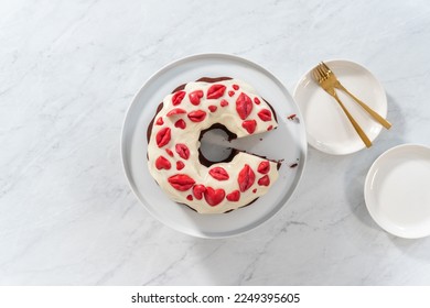 Flat lay. Slicing freshly baked red velvet bundt cake with chocolate lips and hearts over cream cheese glaze for Valentine's Day. - Shutterstock ID 2249395605