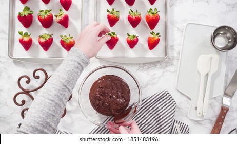Flat lay. Step by step. Dipping organic strawberries into a bowl with melted chocolate to prepare chocolate covered strawberries.