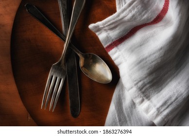 Flat lay still life of old silverware on a round wooden platter with tea towel. 