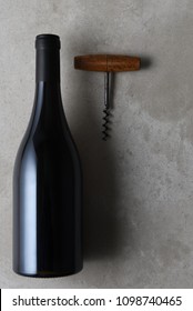 Flat lay still life of a pinot noir shaped wine bottle with cork screw on a concrete table with copy space.