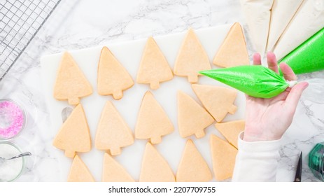 Flat lay. Stp by step. Icing Christmas tree-shaped sugar cookies with green royal icing.