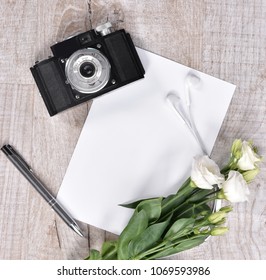  Flat lay style with camera, roses, notebook, earphones and pen on a wooden background. Top view, flat lay. 