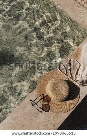 Flat lay of sunglasses and straw hat on marble swimming pool side with clear blue water with waves sunlight shadow reflections. Minimal fashion aesthetic summer vacation top view creative background 商業照片 © 