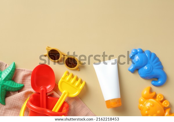 Flat lay sunscreen lotion for kids,\
sunglasses, sand molds, towel on beige\
background.