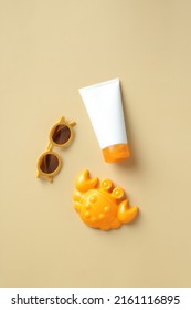 Flat Lay Sunscreen Lotion Tube, Kids Sunglasses And Crab Sandbox Toy On Beige Table. Infant Skin Care, Sun Protection Concept.